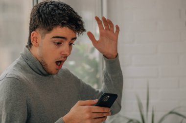 young man at home looking at mobile phone surprised