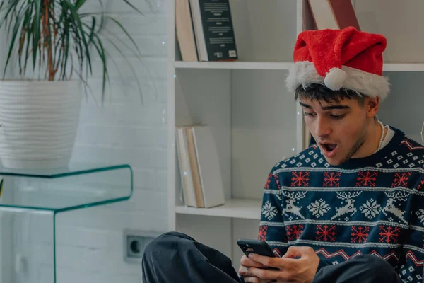携帯電話を見てクリスマスの服を着た若い男が驚いて — ストック写真
