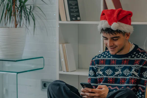 Fiatal Férfi Otthon Karácsonyi Ruhák Nézi Mobiltelefon — Stock Fotó