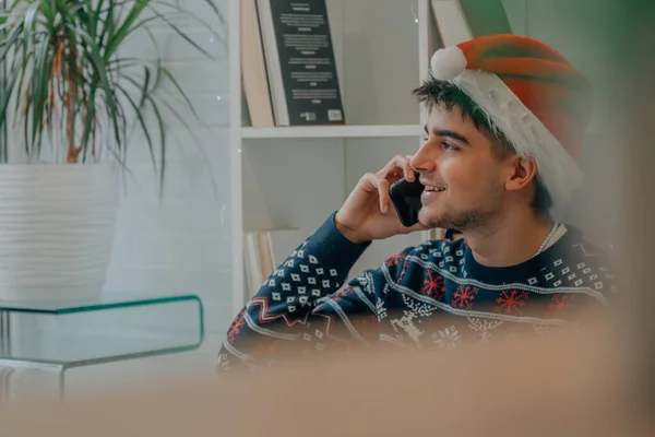 サンタ クラスの帽子とクリスマスの服を携帯電話で話している若い男 — ストック写真