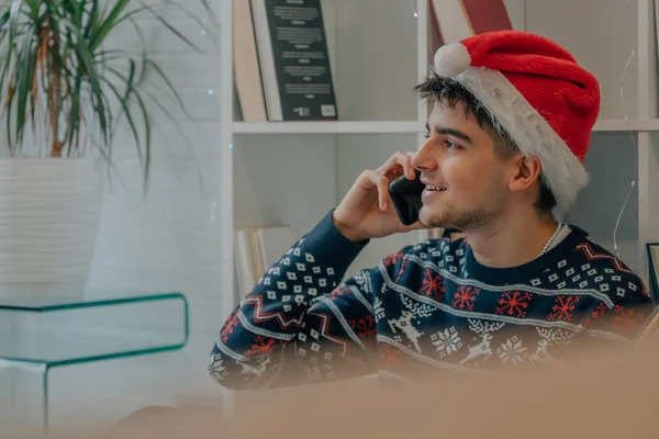 サンタ クラスの帽子とクリスマスの服を携帯電話で話している若い男 — ストック写真