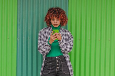 girl with mobile phone in the street with green wall in the background