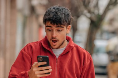 young man with mobile phone in the street with surprised expression
