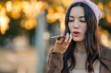 urban young woman in the street with mobile phone and autumn outfit sending or recording voice or audio message