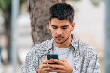 Genç milenyum öğrencisi sokakta cep telefonuna bakıyor.