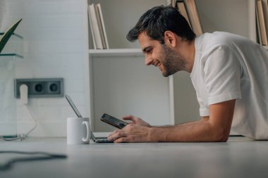 young man at home with mobile phone and laptop on the floor
