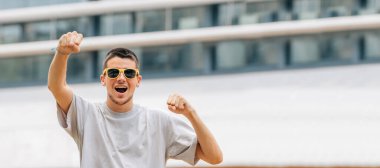Dışarıda güneş gözlüklü genç adam sevinçle kutluyor.
