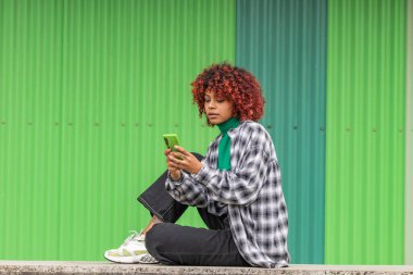 Afro kız sokakta cep telefonuna ya da cep telefonuna bakıyor.