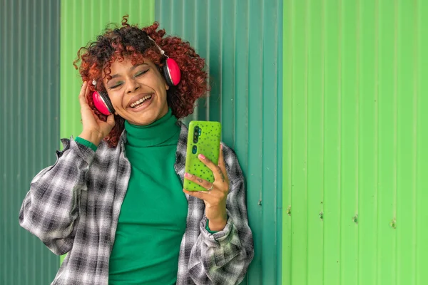stock image afro girl with headphones and phone outdoors on green wall background