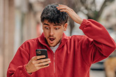 young man with mobile phone in the street with surprised expression