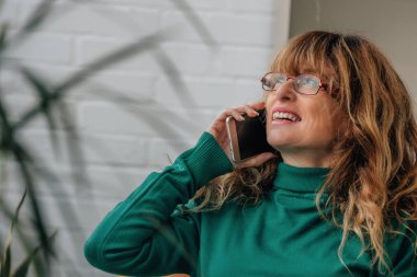 Evde cep telefonuyla konuşan orta yaşlı güzel bir kadın.