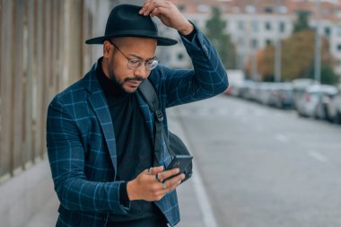 Sokakta cep telefonuna bakan şapkalı Latin bir adam.