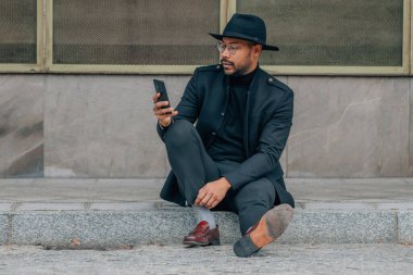 Sokakta cep telefonu olan bir işadamı kaldırımda oturuyor.