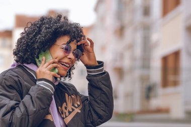 Sokakta güneş gözlüklü afro kız cep telefonuyla konuşuyor.