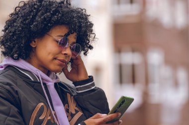 Caddedeki afro kız cep telefonuna bakıyor.