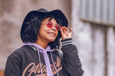 Şapkalı ve güneş gözlüklü kız gülümsüyor.