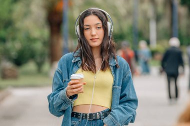 Kulaklıklar ve bir fincan kahveyle yürüyen kız.