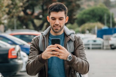 Sokakta cep telefonu ve sırt çantalı bir adam var.