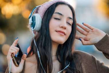 Kışın dışarıda kulaklıklı ve cep telefonlu bir kız.