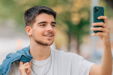 Sokakta telefonlu genç bir adam selfie ya da fotoğraf çekiyor.