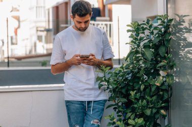 Evinin terasında cep telefonlu bir gencin şehir manzarası