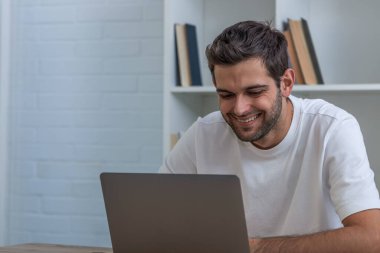 Masasında dizüstü bilgisayarı olan genç bir adam.