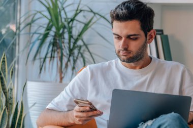 Evde bilgisayar ve cep telefonu olan genç bir adam.