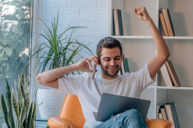 Bilgisayarlı ve cep telefonlu genç adam başarısını ve neşesini ifade ediyor