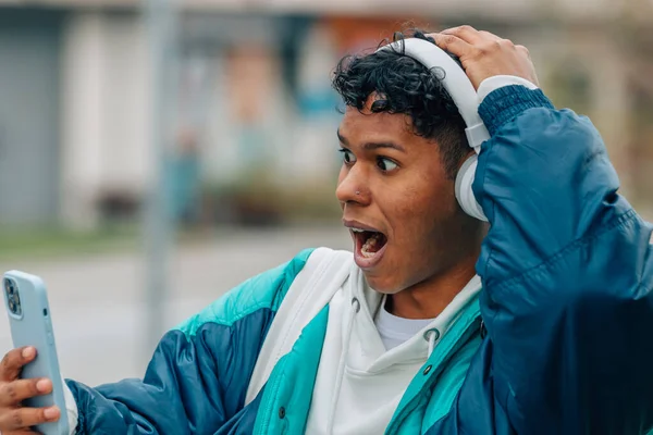 Fiatal Férfi Fejhallgatóval Mobiltelefonnal Meglepett Arckifejezéssel — Stock Fotó