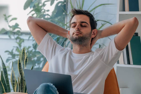 Genç adam evinde bilgisayar başında kanepede dinleniyor.