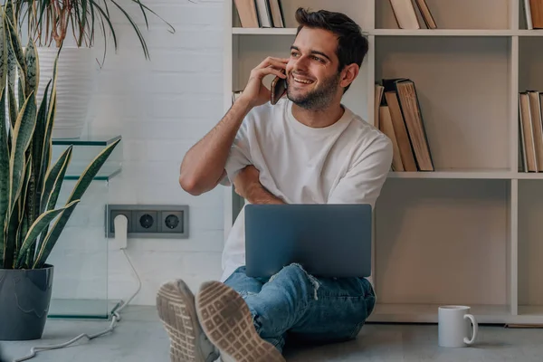 stock image young man at home with laptop talking on mobile phone