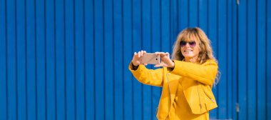 orta yaşlı bir kadın cep telefonuyla selfie çekiyor.