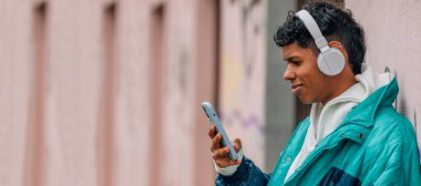 Sokakta cep telefonu ve kulaklığı olan genç bir adam.