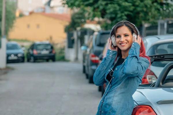 smiling girl with headphones on the street next to the car