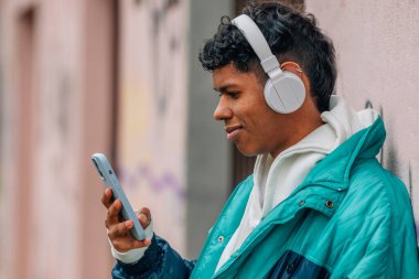 Sokakta cep telefonu ve kulaklığı olan genç Latin bir adam.