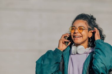 Gözlüklü kız sokakta cep telefonuyla konuşuyor.