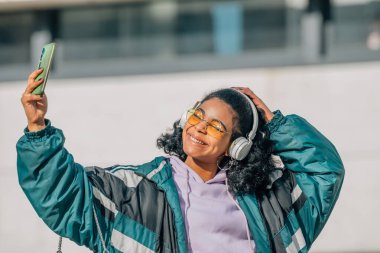 Cep telefonlu kız sokakta selfie ve kulaklık yapıyor.