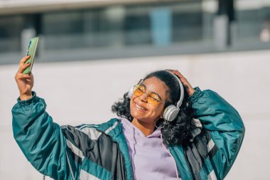 Cep telefonlu kız sokakta selfie ve kulaklık yapıyor.