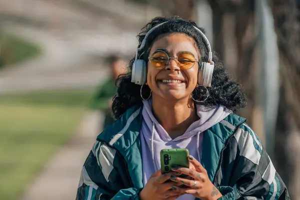 happy smiling girl with headphones and mobile phone listening to music on the street