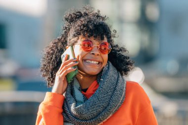 Sokakta güneş gözlüklü kız cep telefonuyla konuşuyor.