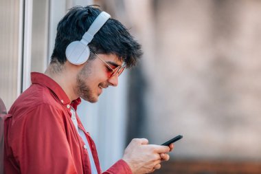 Profilde kulaklık ve cep telefonu olan genç bir adam.