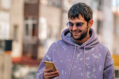 Dışarıda güneş gözlüklü ve cep telefonlu genç bir adamın portresi.