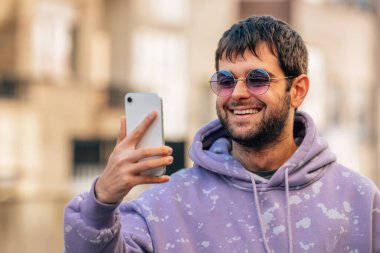 Dışarıda güneş gözlüklü ve cep telefonlu genç bir adamın portresi.