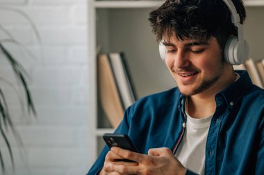 Evde cep telefonu ve kulaklığı olan genç bir adam.