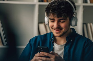 Evde kulaklığı ve cep telefonu olan genç bir adam.