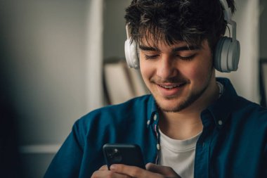 Evde kulaklığı ve cep telefonu olan genç bir adam.