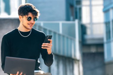 Dizüstü bilgisayarı ve cep telefonu olan genç bir adam.