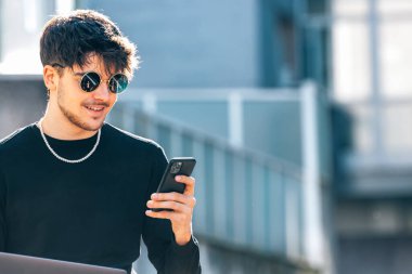 Dışarıda cep telefonu ve dizüstü bilgisayarı olan genç bir erkek.