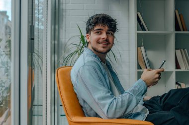 Evdeki kanepede cep telefonu ya da akıllı telefonu olan genç bir adam.