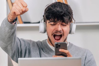 Masasında kulaklık, cep telefonu ve dizüstü bilgisayarı olan bir öğrenci var.